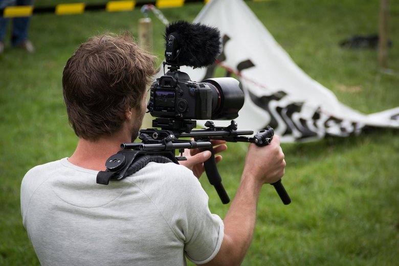 Un homme porte une caméra sur son épaule droite pour filmer