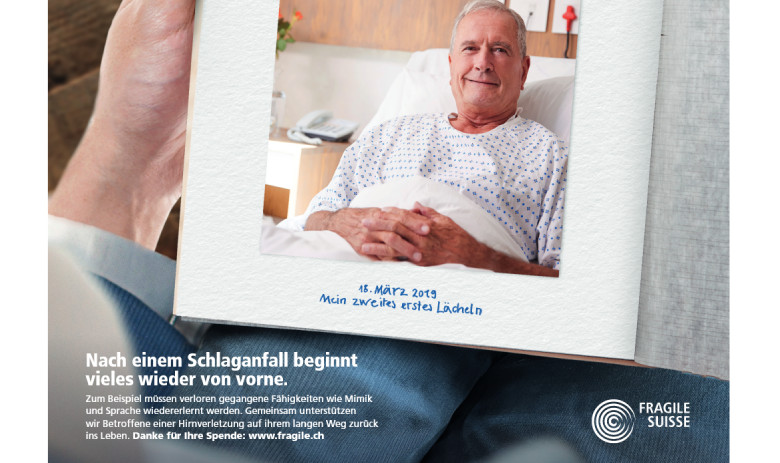 Füllerinserat von vorne beginnen Ein Inserat von FRAGILE Suisse. Eine Person hat ein offenes Tagebuch auf den Knien, darin ein Foto eines älteren Mannes im Bett, der in die Kamera lächelt. Daruntre steht: 18. März 2019: Mein zweites erste Lächeln.