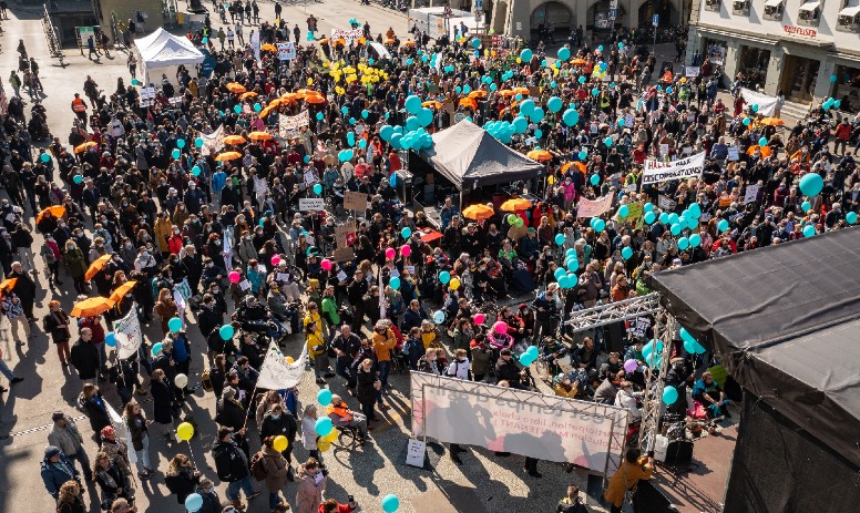 Kundgebung in Bern Aufnahme von oben: Viele Menschen stehen versammelt auf einem Platz und halten Schilder und Luftballons in die Höhe