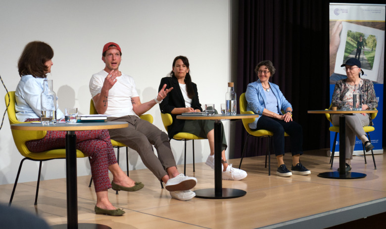Podiumsdiskussion mit Kevin Lötscher Fünf Personen sitzen verteilt an drei Tischen auf einer Bühne.