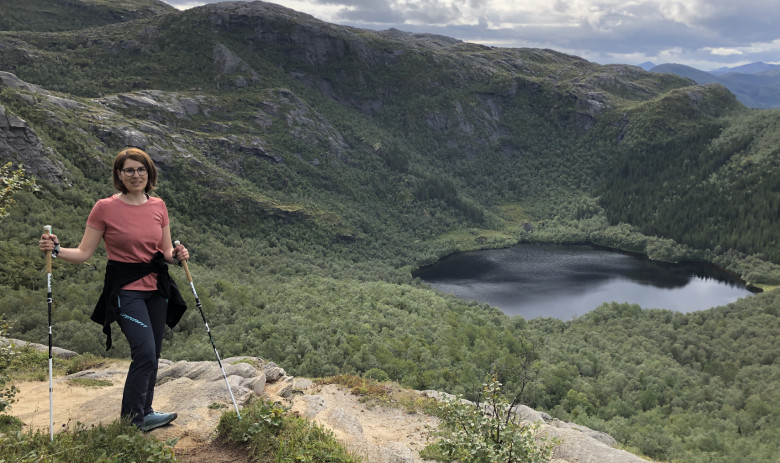 Sandra S. Eine Person mit Wanderstock steht in der nähe eines Berghangs. Ein wunderbarer Blick auf einen Bergsee im Hintergrund