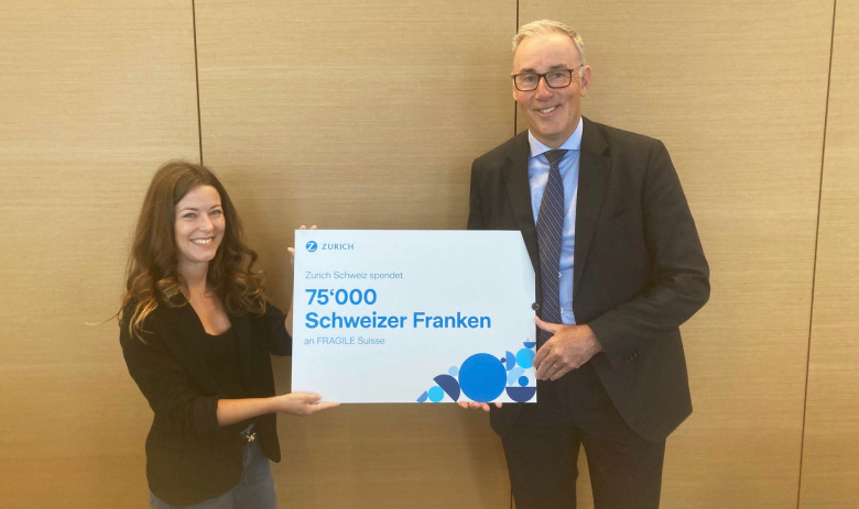Checkübergabe Eine Frau und ein Mann posieren für ein Foto und halten gemeinsam einen grossen Check. Darauf steht: Zurich Schweiz spendet 75'000 Schweizer Franken an FRAGILE Suisse