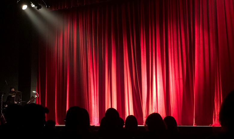 Théâtre Spectateurs sont de dos et regardent la scène et ses grands rideaux rouges
