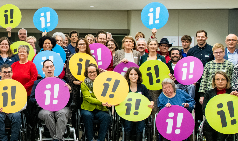 Inklusions-Initiative Gruppenfoto. Zahlreiche Personen halten bunte Logos der Inklusions-Initiative hoch.
