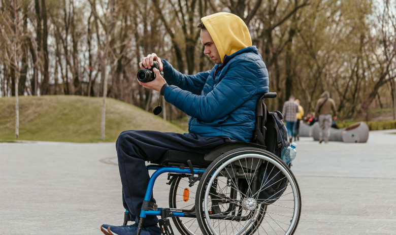 Reporter:innen ohne Barrieren Eine Person im Rollstuhl macht ein Foto mit einer Spiegelreflexkamera