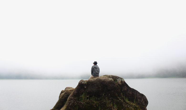 Stille Ein Mensch sitzt auf einem Felsen in einem Nebelmeer.