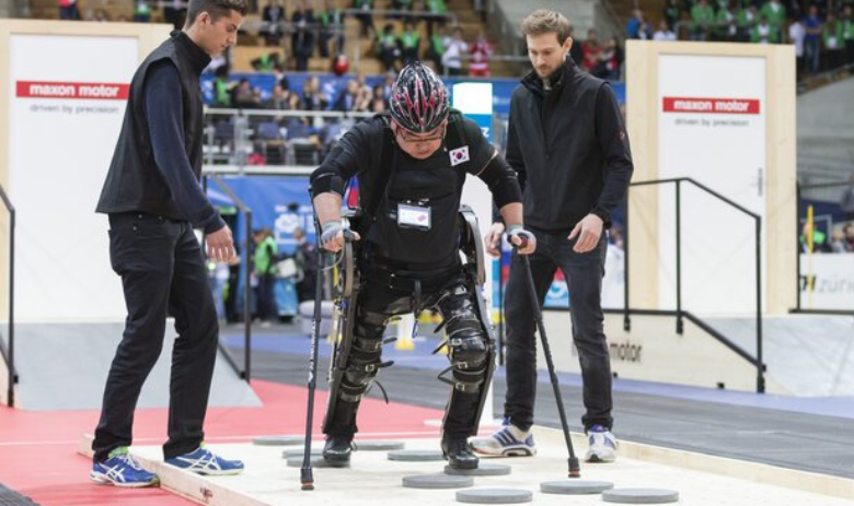 Cybathlon 2024 Drei Personen, in der Mitte Mann mit Gehhilfe, der an einer Cybathlon Disziplin teilnimmt